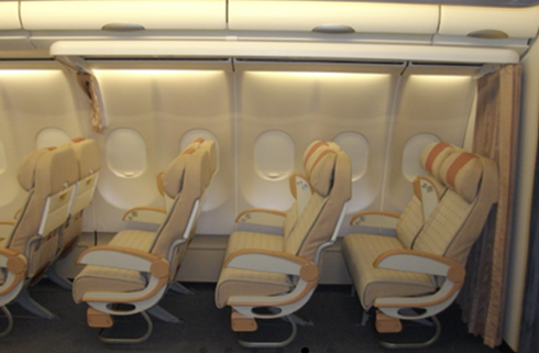 Row of four airplane seats with beige cushioning and brown accents, positioned next to large oval windows, conveying a calm and orderly atmosphere.
