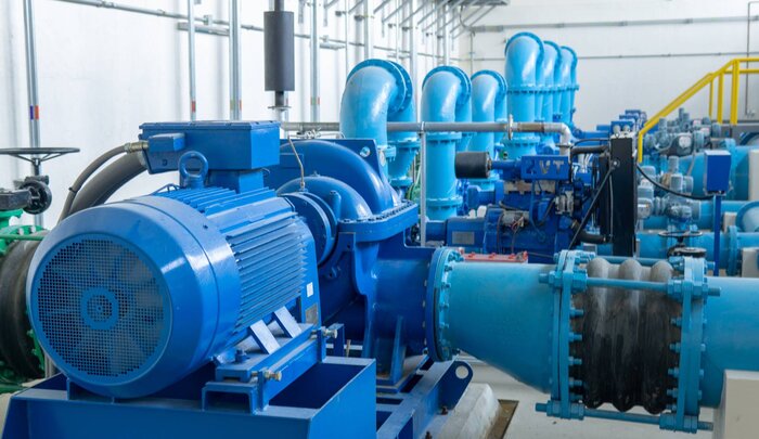 Eine Reihe von großen blauen Wasserpumpen mit Motoren und Rohrleitungen in einer technischen Anlage.