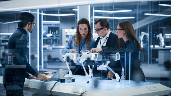 Vier Personen stehen um einen Tisch in einem Hightech-Labor und betrachten einen vierbeinigen Roboter.