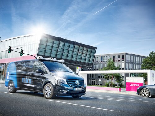 Ein schwarz und blau lackierter Van fährt vor einem modernen Bürogebäude der Telekom.