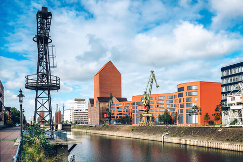 Ein Blick auf den Düsseldorfer Medienhafen mit roten Gebäuden, Kränen und Wasserkanal.