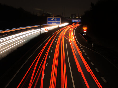 Eine Autobahn bei Nacht mit roten und weißen Lichtspuren der Fahrzeuge.