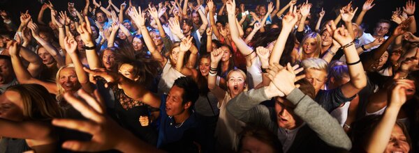 Große Menschenmenge auf einer Party oder einem Konzert, alle strecken die Arme in die Luft.