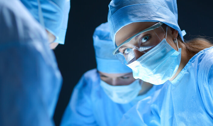 Chirurgisches Team in blauer OP-Kleidung mit Mundschutz und Schutzbrillen.