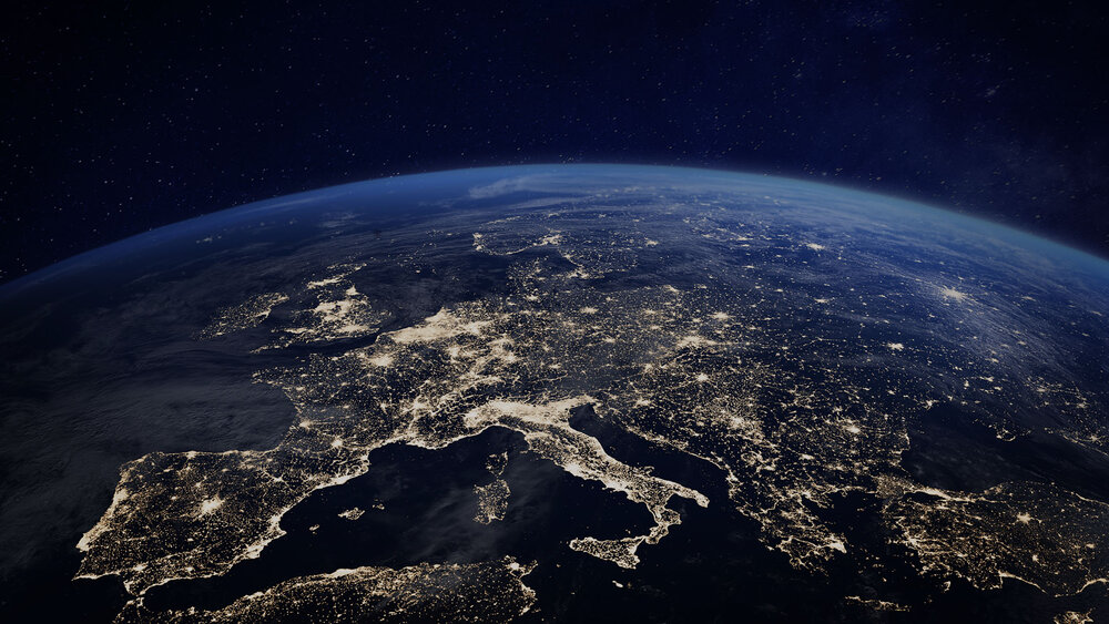 A computer-generated satellite view of Europa at night, showing city lights, with the night sky and twinkling stars in the background.