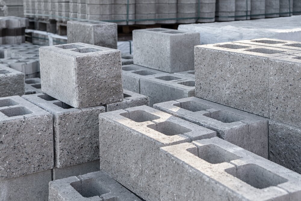 Many grey rectangular hollow concrete blocks are stacked on pallets.