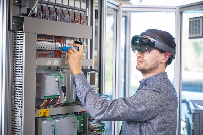 Ein Mann arbeitet mit einem Schraubendreher am Schaltschrank und trägt eine Augmented-Reality-Brille.