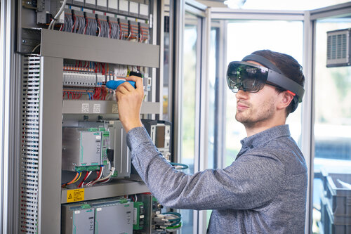 Ein Mann arbeitet mit einem Schraubendreher am Schaltschrank und trägt eine Augmented-Reality-Brille.
