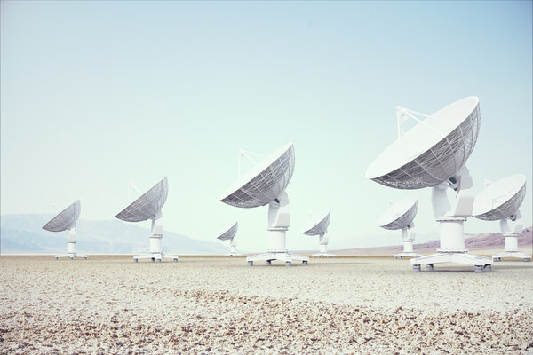 A series of large satellite dishes stand in a desert landscape under a clear blue sky, conveying a sense of isolation and advanced technology.