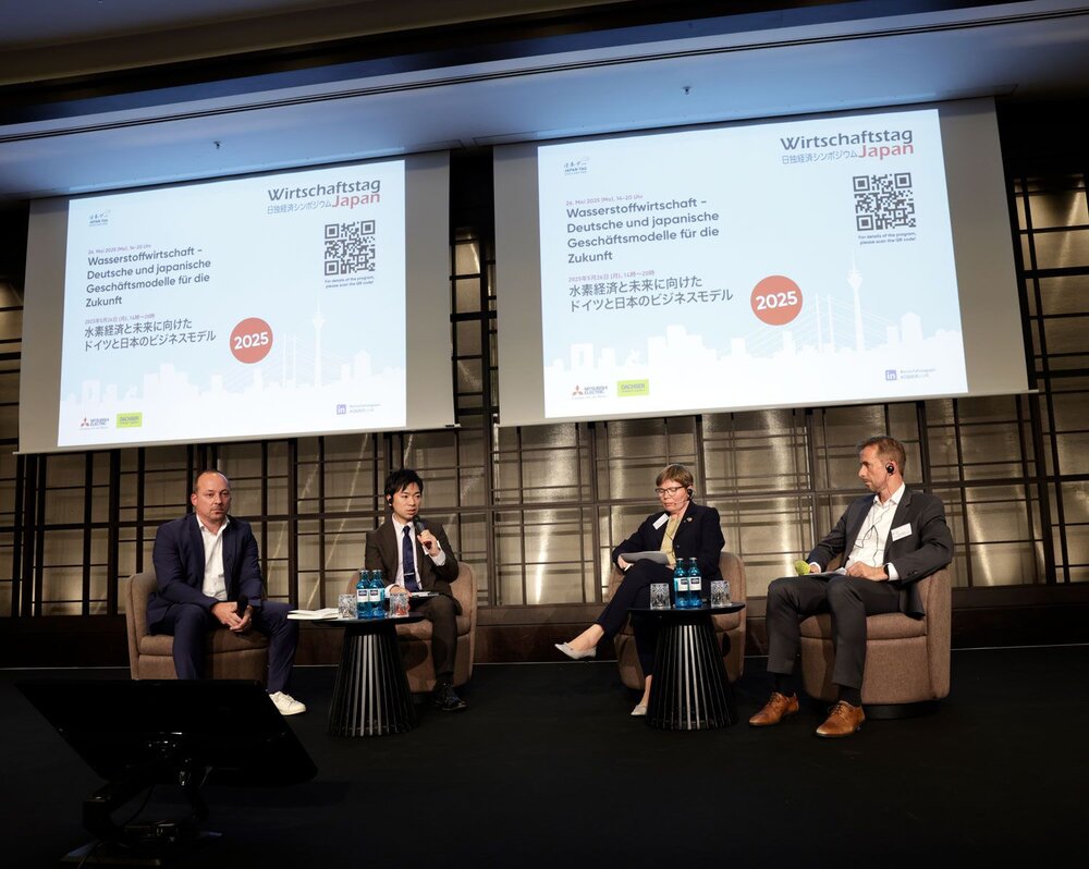Vier Personen in Businesskleidung sitzen auf einer Bühne in Sesseln, hinter ihnen Projektionen mit dem Schriftzug Wirtschaftstag Japan 2025.