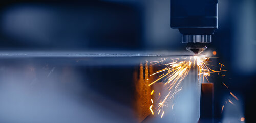 Nahaufnahme eines Laserschneiders, der Funken sprühend eine Metallplatte bearbeitet.
