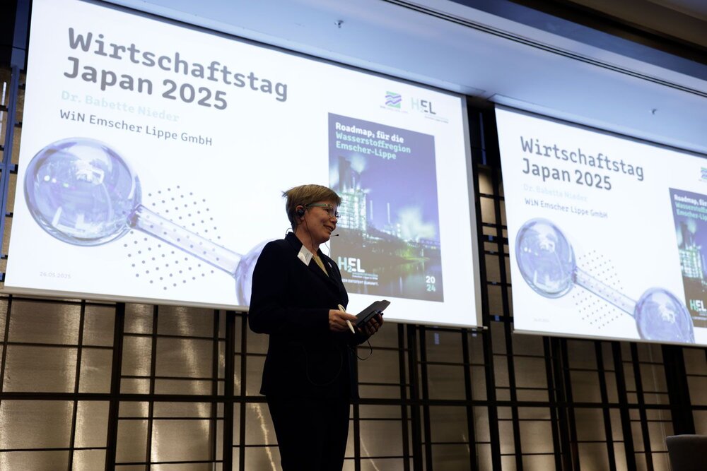 Eine Frau in Businesskleidung mit Headset steht auf einer Bühne, hinter ihr Projektionen mit dem Schriftzug Wirtschaftstag Japan 2025.