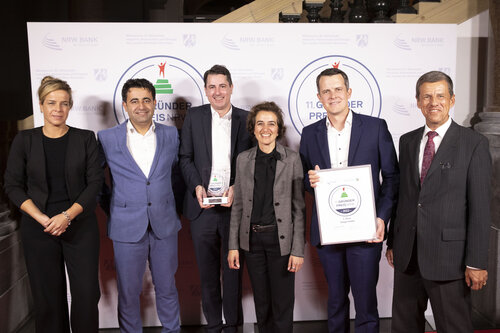 Gruppenfoto bei einer Preisverleihung, sechs Personen in formeller Kleidung, zwei halten eine Urkunde und Trophäe des Gründerpreis NRW.