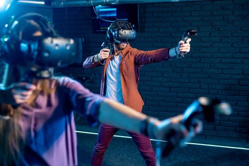 Zwei Personen sind in einem dunklen Raum mit Virtual Reality-Brillen und Controllern und stehen in einer Bogenschuss-Position.