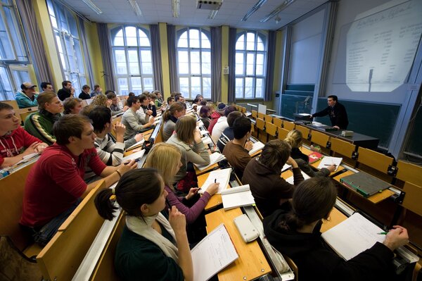 Ein Hörsaal, in dem viele Studierende in mehreren Reihen nebeneinander sitzen und Notizen machen.