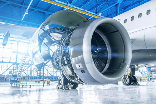 Close-up of a jet engine under maintenance in a bright hangar. The engine's outer casing is removed, revealing intricate machinery inside.