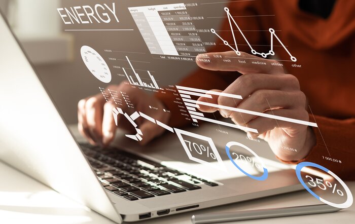 Hände tippen auf einem Laptop, davor sind Energie-Daten in Form von Diagrammen und Prozentwerten als Hologramm eingeblendet.