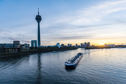 Ein Blick auf den Rhein mit einem vorbeifahrendem Schiff, Fernsehturm und Skyline von Düsseldorf bei Sonnenuntergang.