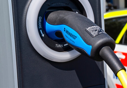 Eine Nahaufnahme eines schwarz-blauen Ladesteckers von Mennekes, eingesteckt in eine schwarze E-Ladestation mit Drehmechanismus.