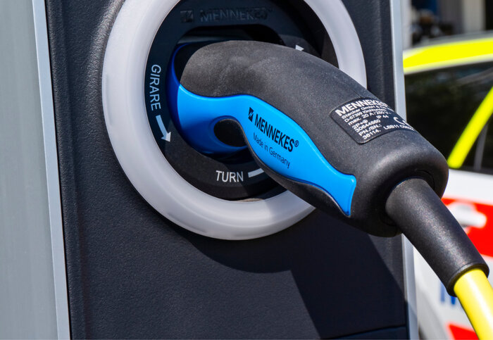 Eine Nahaufnahme eines schwarz-blauen Ladesteckers von Mennekes, eingesteckt in eine schwarze E-Ladestation mit Drehmechanismus.