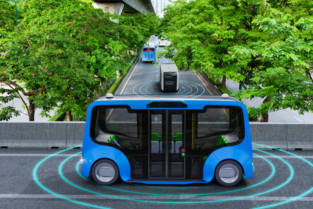 Autonomous blue shuttles drive on a tree-lined street, surrounded by digital waves indicating connectivity. The scene is modern and innovative.