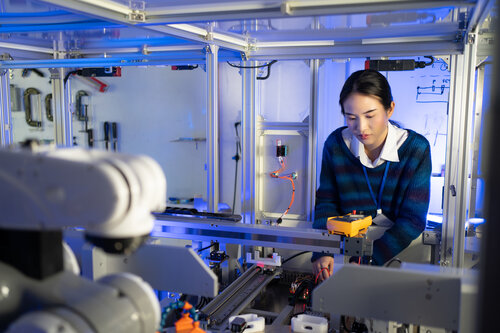 Eine Frau in einem Labor an einer automatisierten Maschine mit Roboterarm und weiteren elektronischen Komponenten.