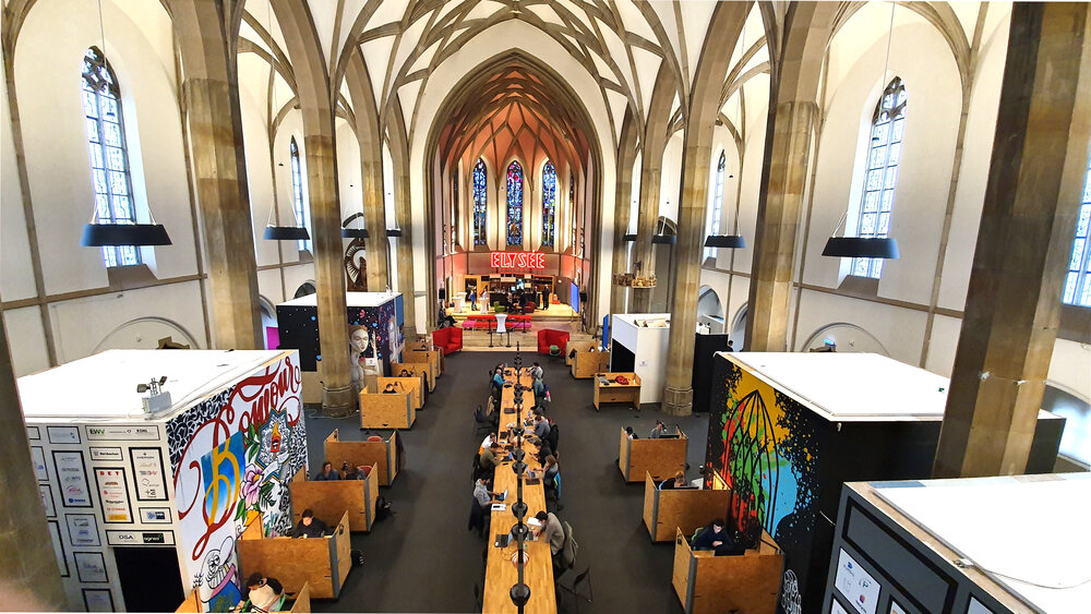 An interior shot of a church with high vaulted ceilings, long work tables, and cubicles, used as a modern coworking space.