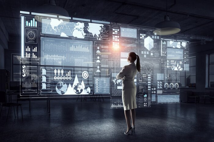 Eine Frau betrachtet eine große, holografische Datenwand mit Diagrammen, Karten und Statistiken.