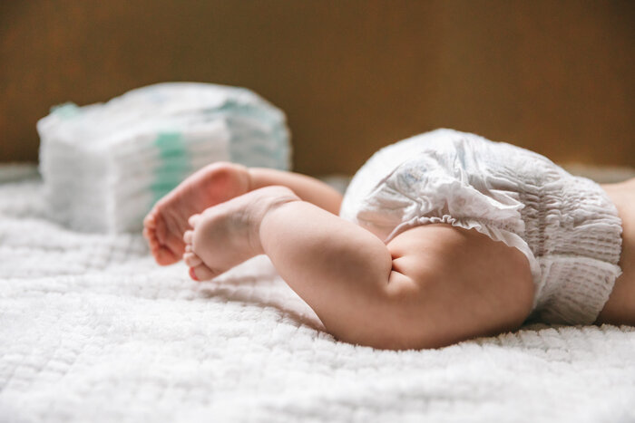 Ein Baby mit Windel liegt auf einer Decke, im Hintergrund ein Stapel weiterer Windeln.