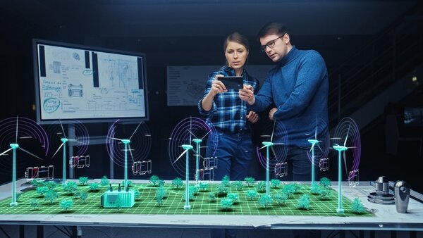 Zwei Personen schauen auf ein Smartphone, über einem Tisch vor ihnen ist ein Hologramm eines Windparks.