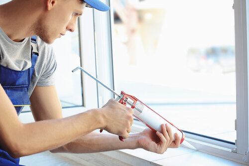 Ein Handwerker trägt Dichtmittel mit einer Kartuschenpistole an einem Fensterrahmen auf.