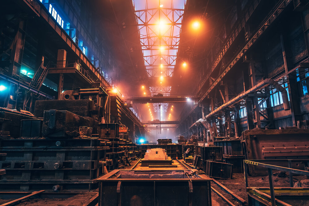 A large industrial hall with heavy machinery, rails and yellowish-orange lighting under the ceiling.