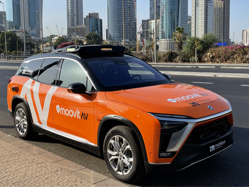 Orangefarbenes autonomes Auto von MoovitAV und Mobileye, geparkt vor modernen Hochhäusern.
