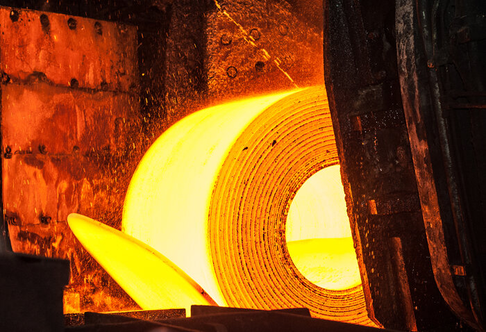 Ein glühend heißes Stahlband in einer Industrieanlage, das zu einer großen Rolle aufgewickelt ist.