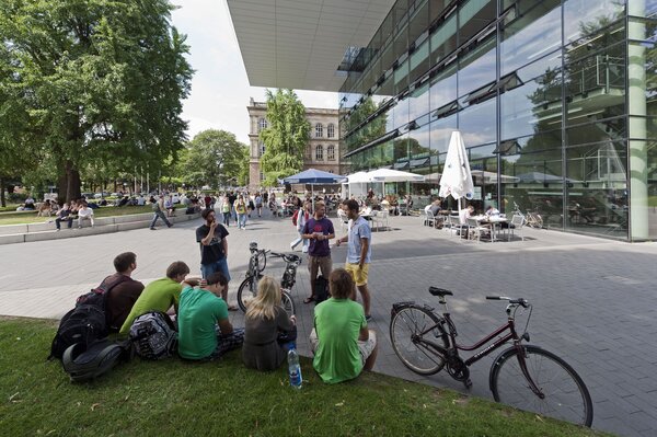 Viele gehende, sitzende oder stehende Studierende vor einem modernen Gebäude der RWTH Aachen, dessen Fassade hauptsächlich aus Fenstern besteht.