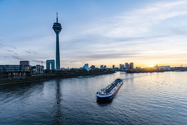 Ein Blick auf den Rhein mit einem vorbeifahrendem Schiff, Fernsehturm und Skyline von Düsseldorf bei Sonnenuntergang.