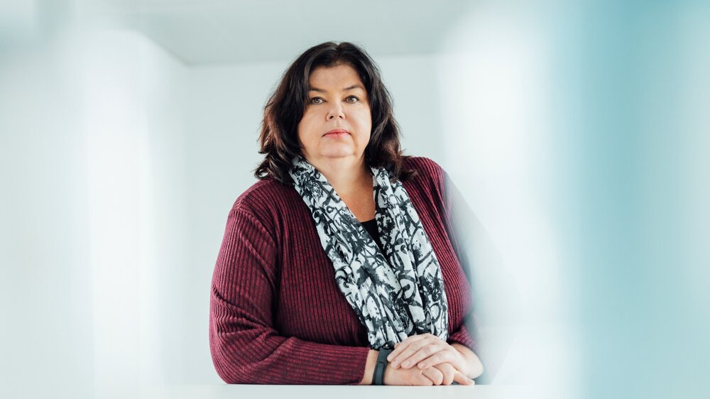 A portrait photograph of a woman sitting behind an office desk wearing a black and white patterned scarf.