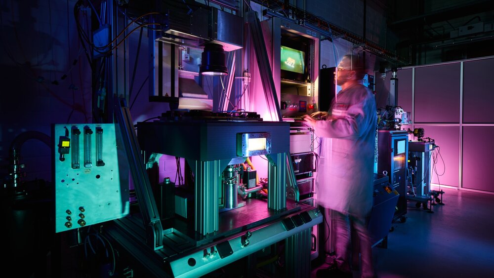 A scientist in a lab coat operates advanced machinery in a dimly lit, neon-lit laboratory, conveying a futuristic and focused atmosphere.