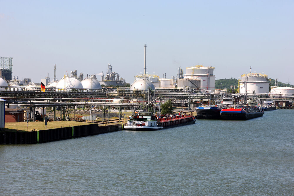 An industrial site with tanks and pipes at a port with cargo ships.