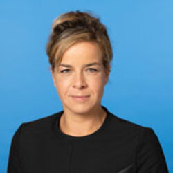 Ein Porträtfoto von einer Frau vor blauem Hintergrund, sie ist in schwarz gekleidet.