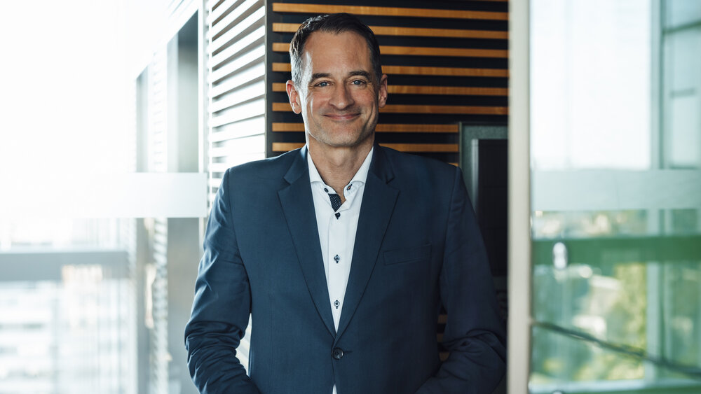 A portrait photograph of a smartly dressed man wearing a white shirt and a dark navy blue jacket.