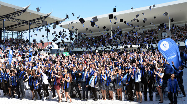 Zahlreiche Menschen werfen bei einem Graduiertenfest ihre Studentenhüte in die Höhe.