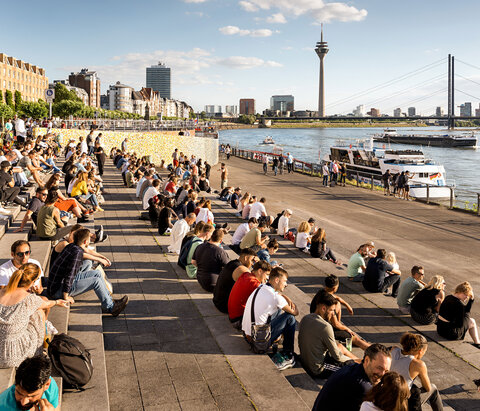Viele Menschen sitzen am Rheinufer in Düsseldorf am Nachmittag bei gutem Wetter.
