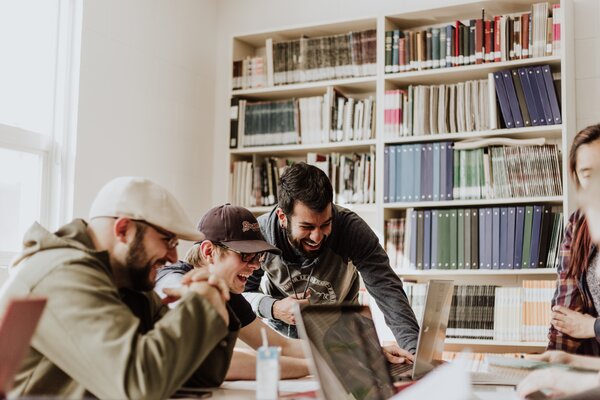 Mehrere junge Menschen arbeiten gemeinsam an einem Tisch mit Laptops.