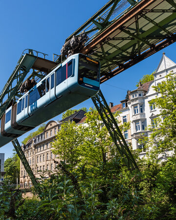 Wuppertaler Schwebebahn fährt auf erhöhter Strecke durch Bäume und Häuser im Bergischen Städtedreieck.
