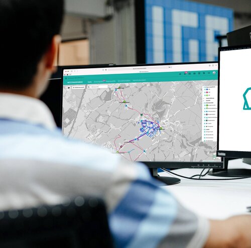 Eine Person betrachtet auf einem Monitor eine digitale Landkarte mit farbigen Markierungen.