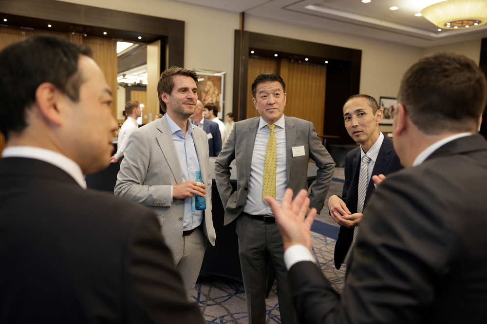 Five men in business attire are engaged in a lively discussion at a networking event. The setting is a conference room with a formal ambiance.