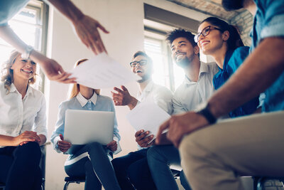 Group of people sitting in a circle in a meeting room with one person handing out papers