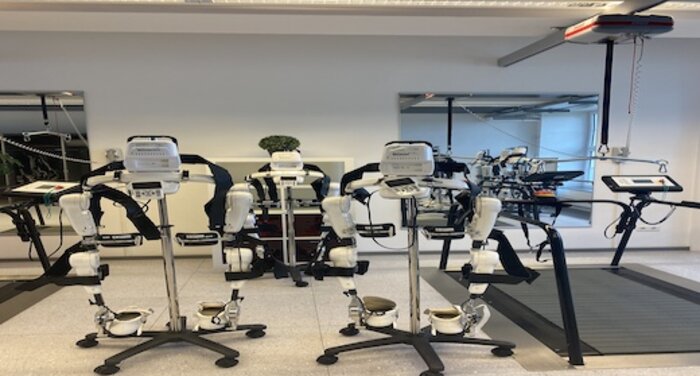 Medizinische Reha-Geräte mit Exoskeletten in einem Trainingsraum mit Spiegeln und Laufbändern.